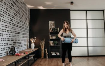 Plus size woman rolling a yoga mat in a stylish indoor setting with modern decor.